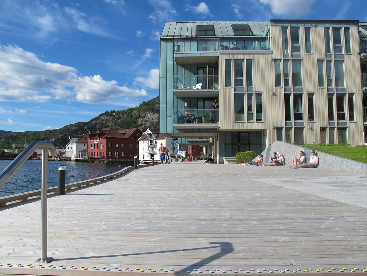 Sandviken sjøfront. Mennesker sitter på brygge med boligblokk bak.